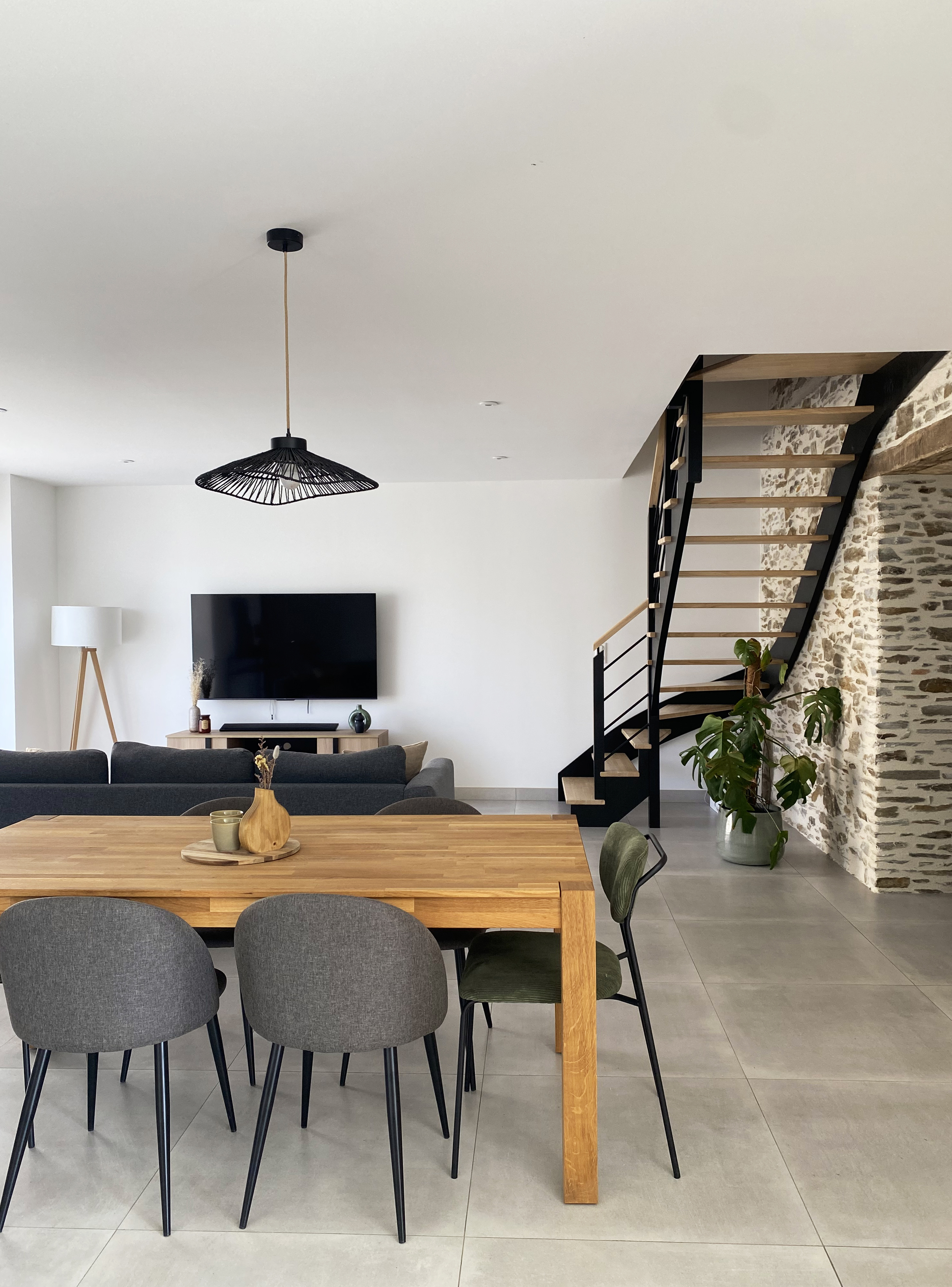 Séjour spacieux avec table en bois, chaises tissu gris vert kaki, mur en pierre et escalier noir — Projet Tremblay